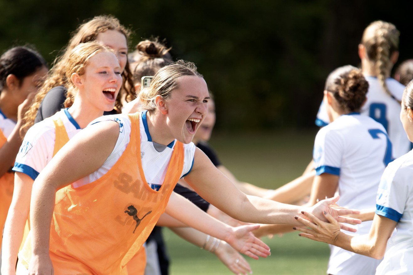 A female soccer player in an orange jersey greets the opposing team