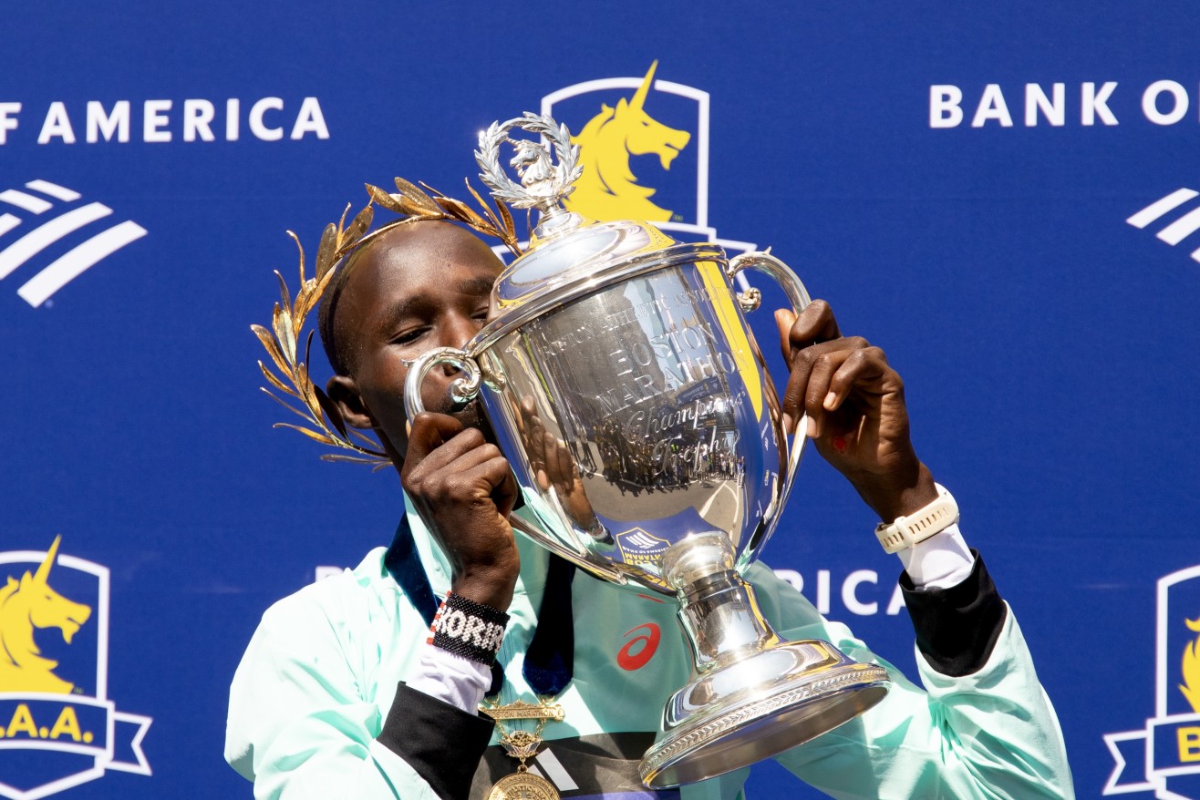 A man in a teal shirt kissing a trophy